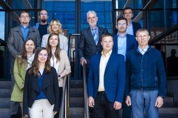 Dziesięć osób stoi na schodzach przeszklonego budynku, pozując do zdjęcia