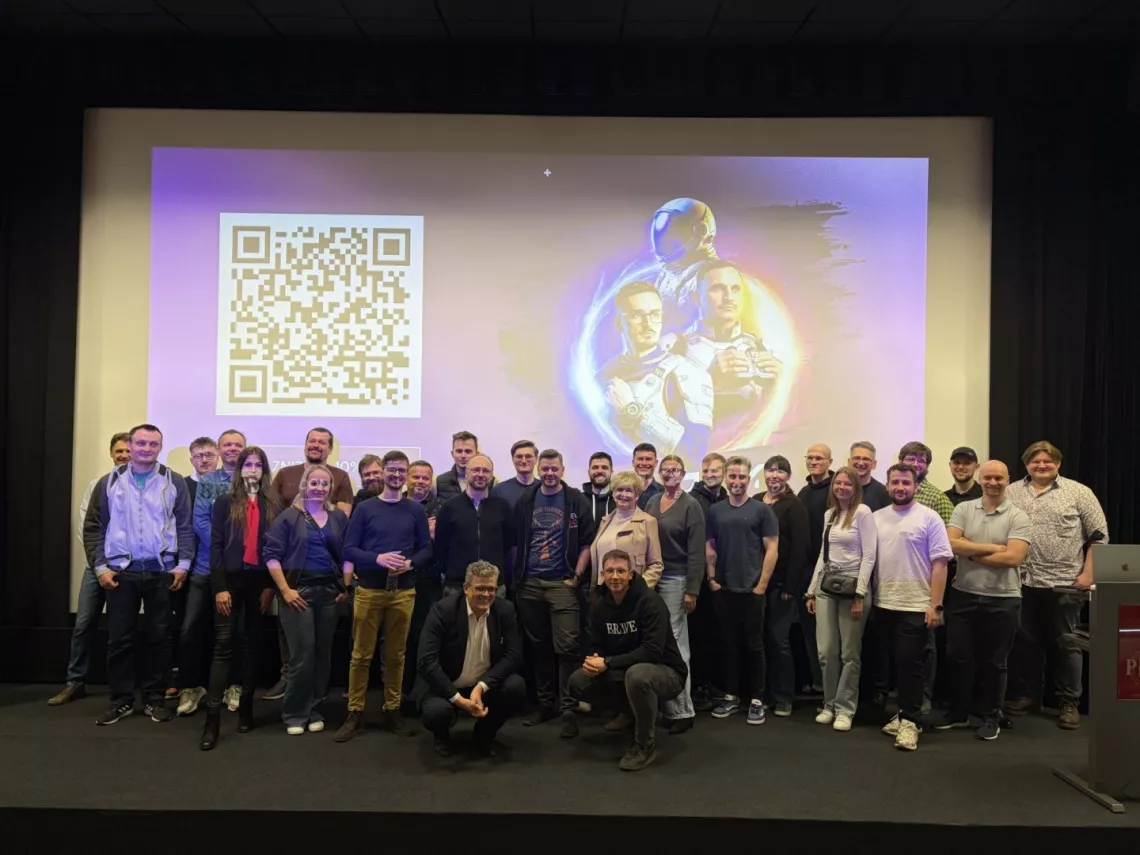 Zdjęcie kilkudziesięciu osób stojacych na scenie, za którymi wyświetla się ekran ze slajdem nawiązującym do wydarzenia