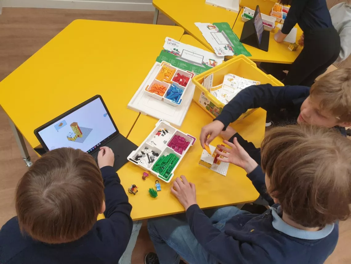 Dzieci siedzą przy stole, na którym leżą klocki do budowania