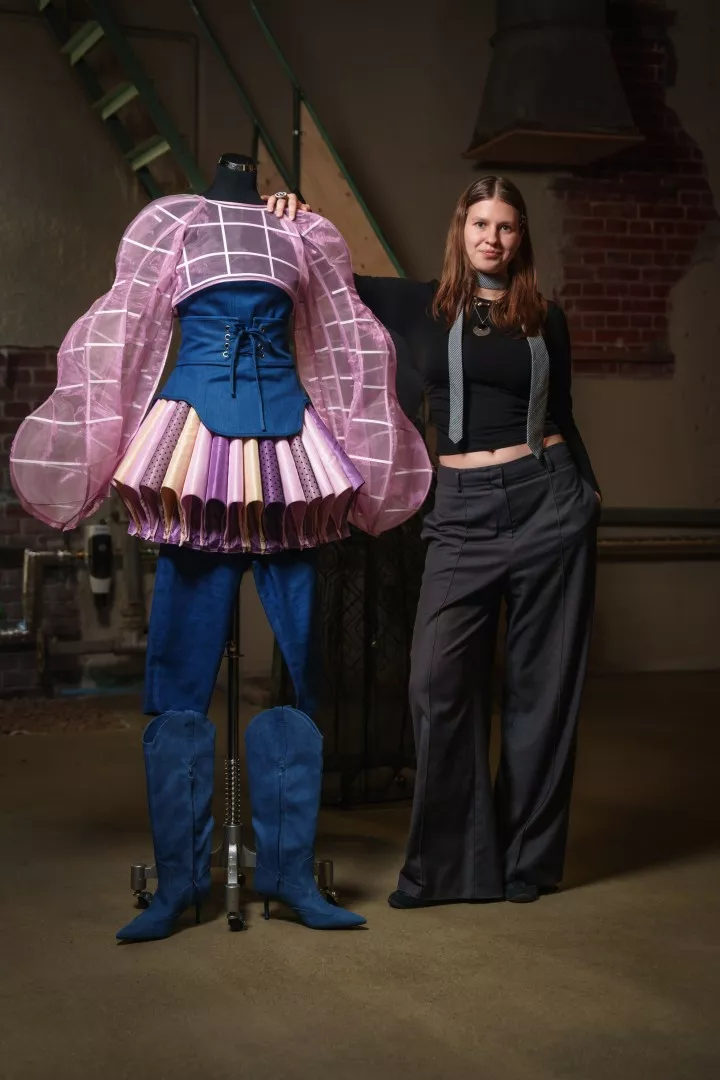Studentka stoi przy zaprojektowanej przez nia futurystycznej sukience z dodatkami