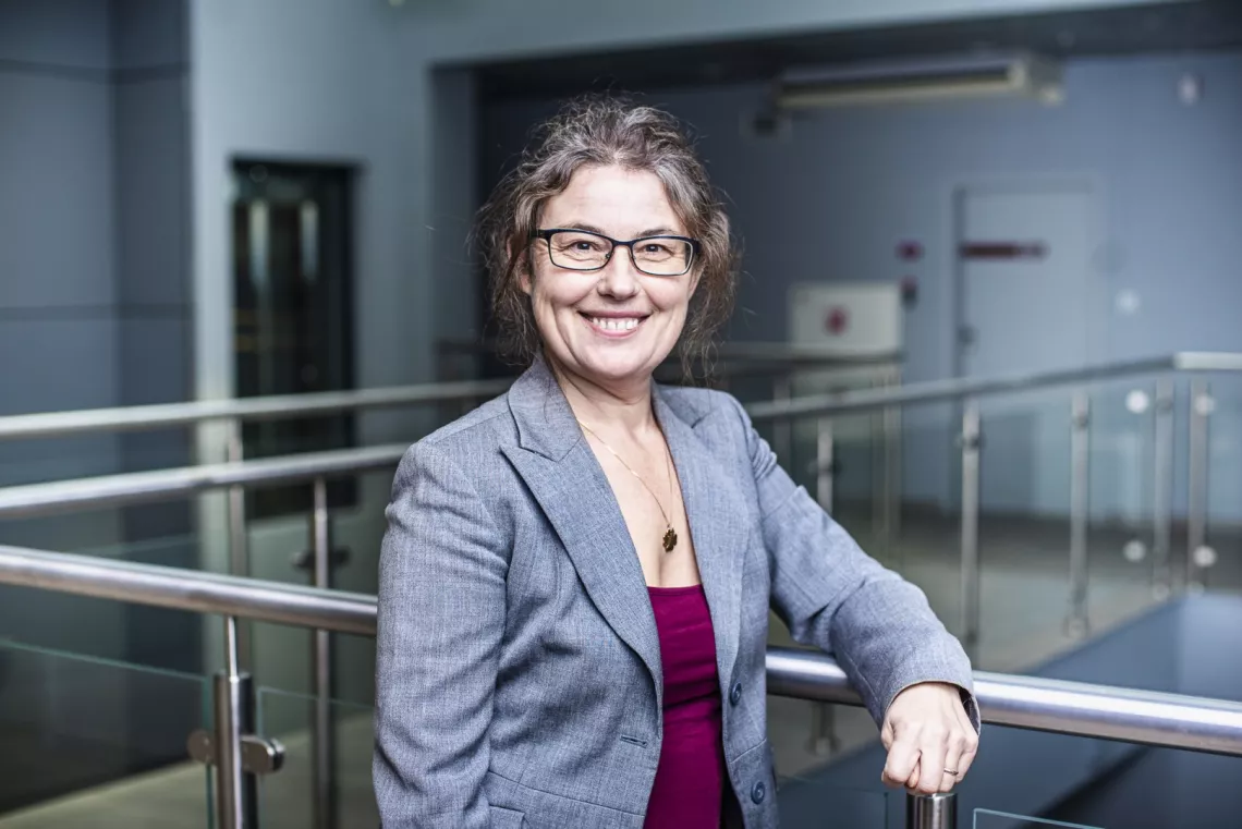 Usmiechnięta kobieta oparta o balustradę w holu budynku