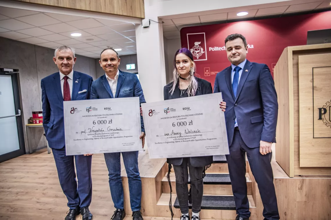 Kobieta i mężczyzna z czekami w ręku obok stoją pomiędzy dwoma mężczyznami