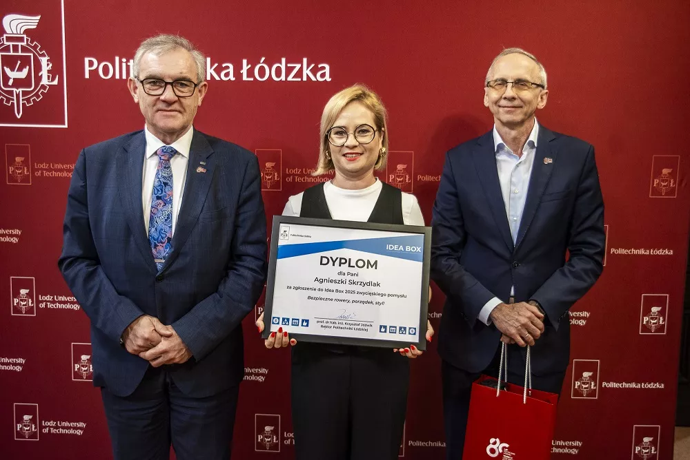 Kobieta tzymająca dyplom w towarzystwie dwóch mężczyzn, stoją na tle bordowego baneru z napisem Politechnika Łódzka