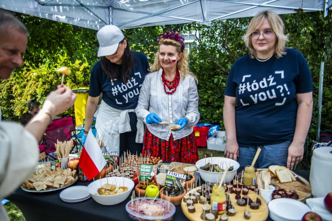 Przy stoisku, na którym są wystawione rózne potrawy stoją trzy kobiety.