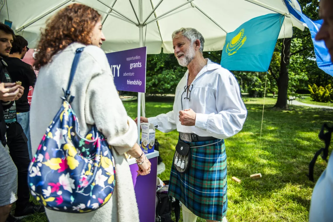 Mężczyzna w szkockim kilcie rozmawia z kobietą w jasnym okryciu.