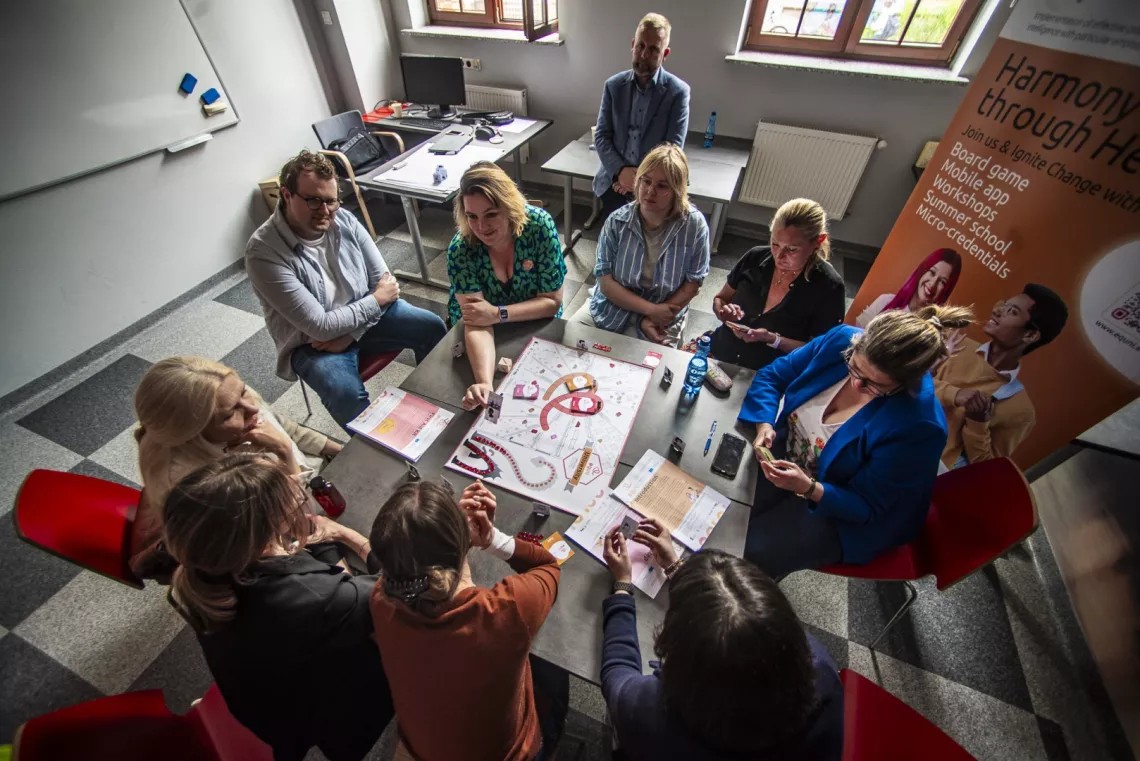 Kilka osób siedzi wokół stołu, na którym jest rozłożona plamsza z grą