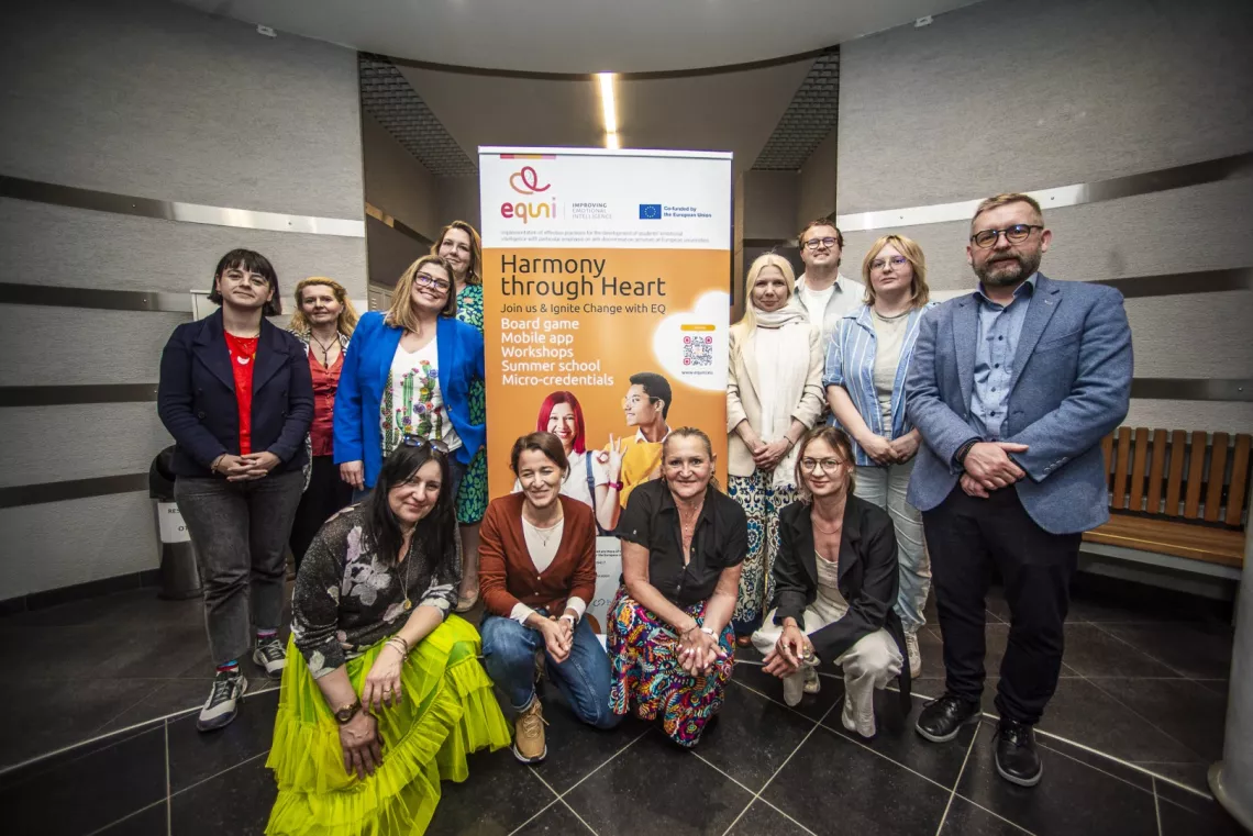 Grupa osób pozuje do zdjęcia, stojąc przy banerze projektu z napisem equni