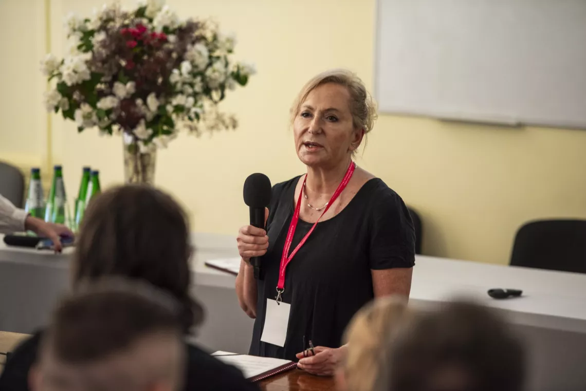 Kobieta trzyma w ręku mikrofon i przemawia do audytorium