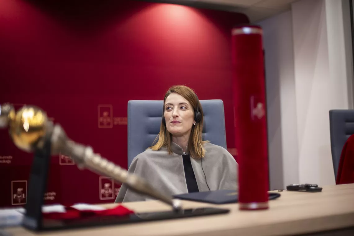 Kobieta w todze siedzi za katedrą w audytorium, na pierwszym planie widoczna tuba oraz berło rektorskie