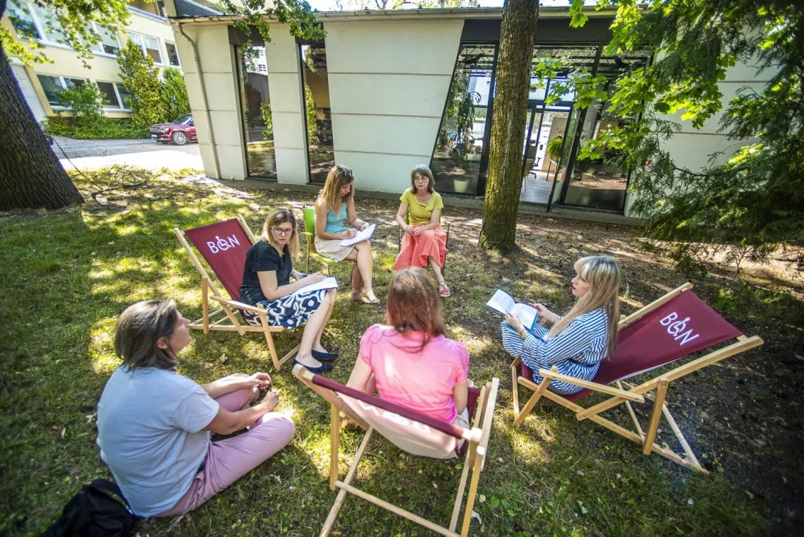 Dyskusja przed budynkiem prowadzona przez kilka kobiet siedzących na leżakach