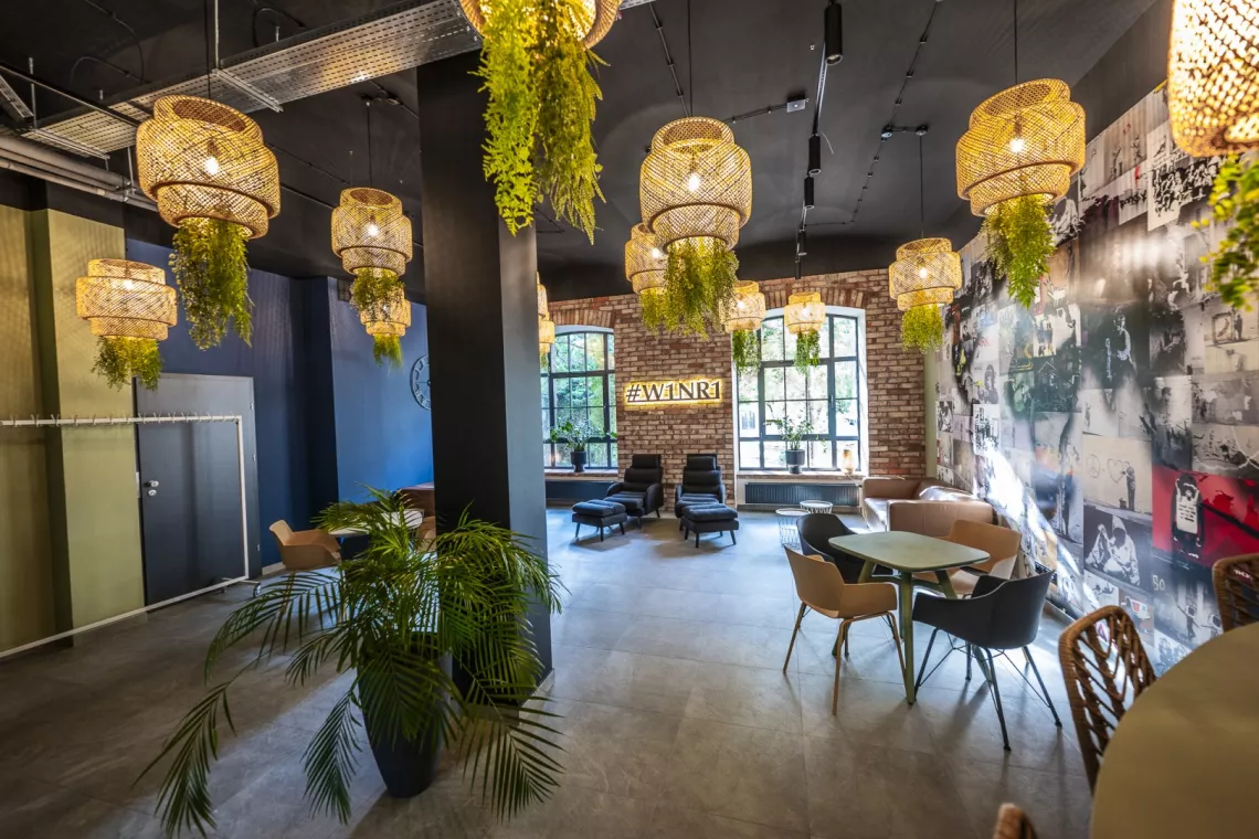 „Nowoczesne wnętrze przestrzeni coworkingowej z różnorodnymi miejscami do siedzenia, roślinami i dekoracjami w stylu industrialnym