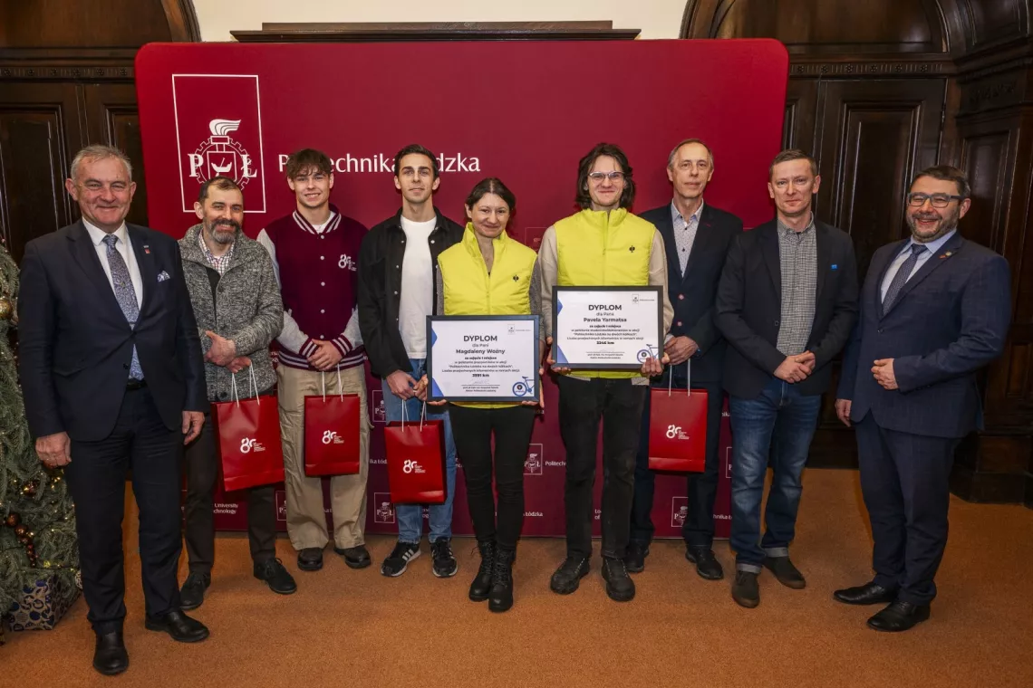 Dziewięc osób, w tym dwie w żóltych kamizelkach, stoją na tle ścianki z napisem Politechnika Łódzka