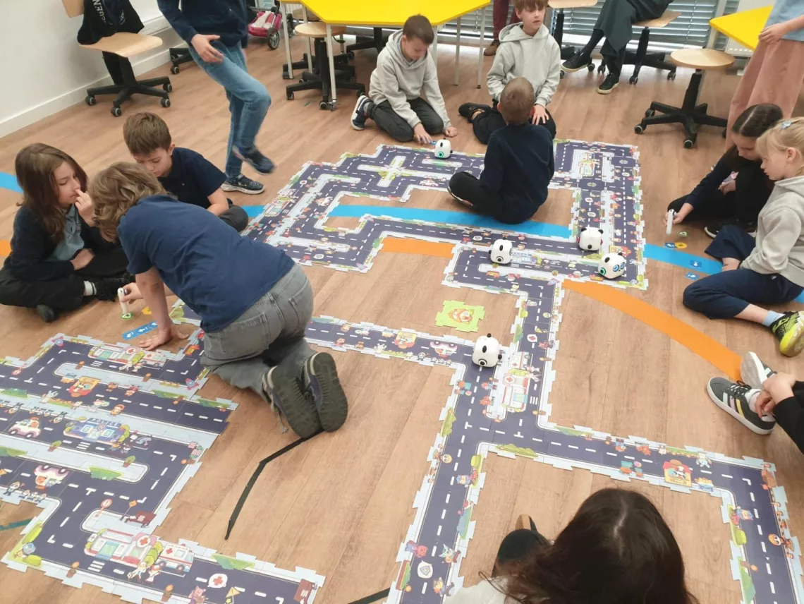 Dzieci nad makietą zrównoważonego miasta - złożonego z puzzli - i poruszające się po nim zaprogramowane roboty