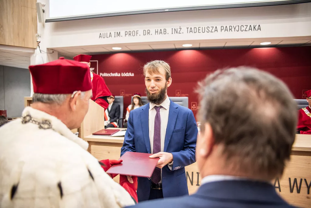 Rektor w paradnym stroju wręcza dyplom młodemu człowiekowi