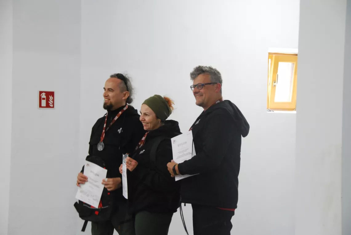 Trzy osoby z medalami i dyplomami pozują do zdjęcia