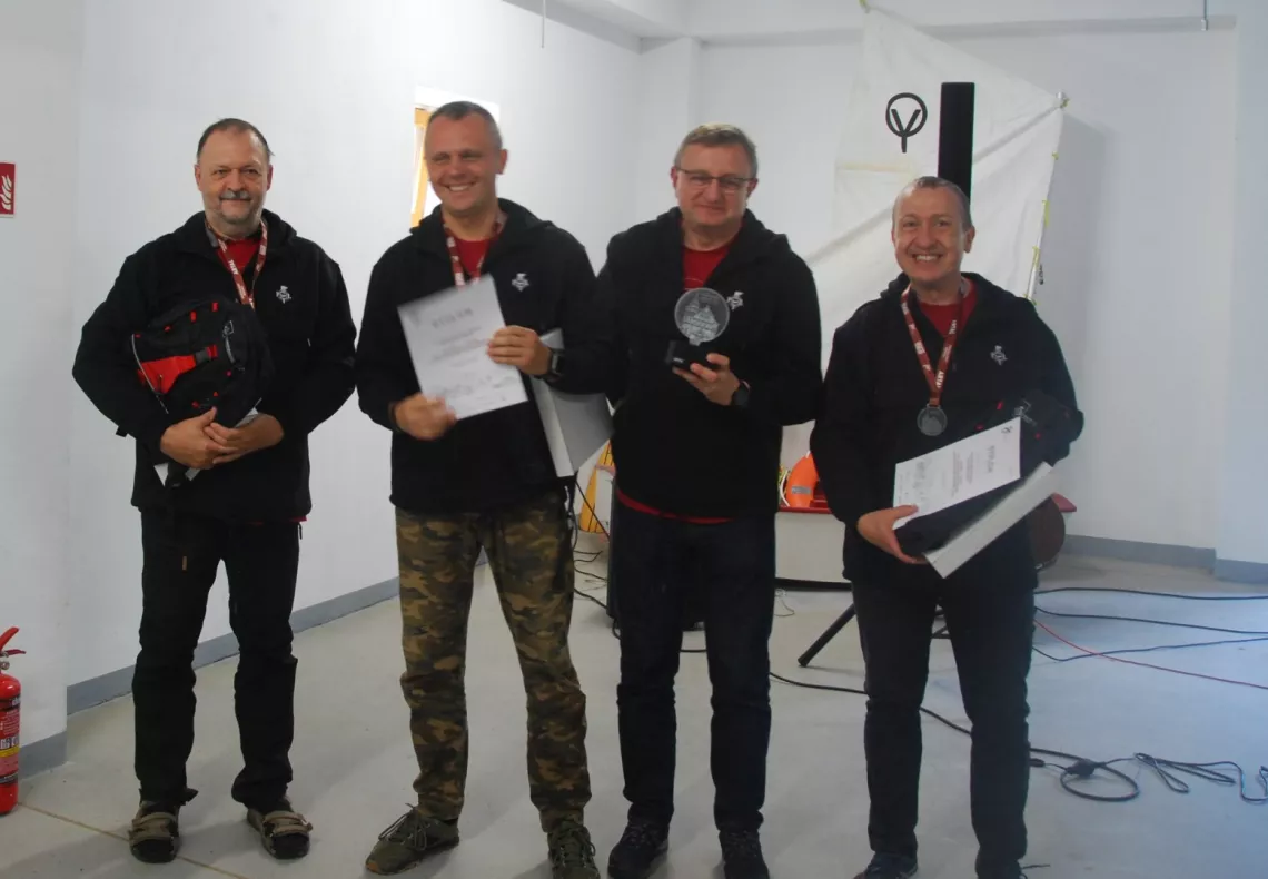 Czterech mężczyzn - trzech ma medal i dyplom, jeden trzyma statuetkę, okazuje radość z otrzymanej nagrody