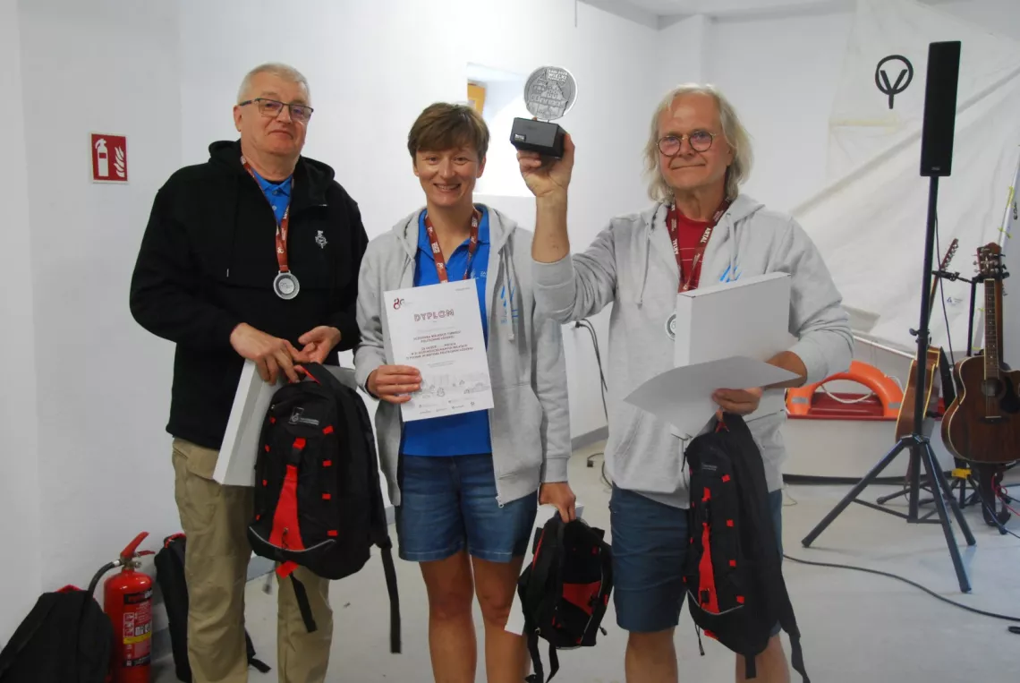 Dwóch mężczyzn i kobieta z dyplomami i nagrodą okazują radość ze zwycięstwa