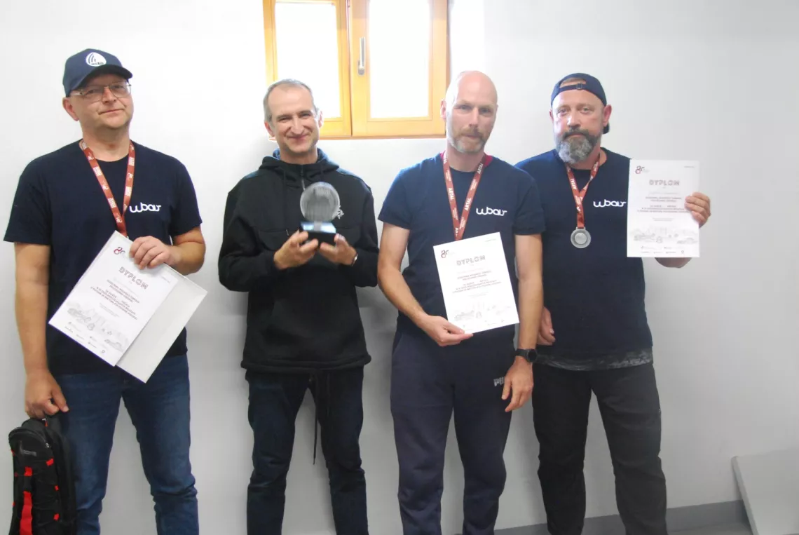 Czterech mężczyzn, trzech ma medale i dyplomy, czwarty trzyma statuetkę z medalami i statuetką