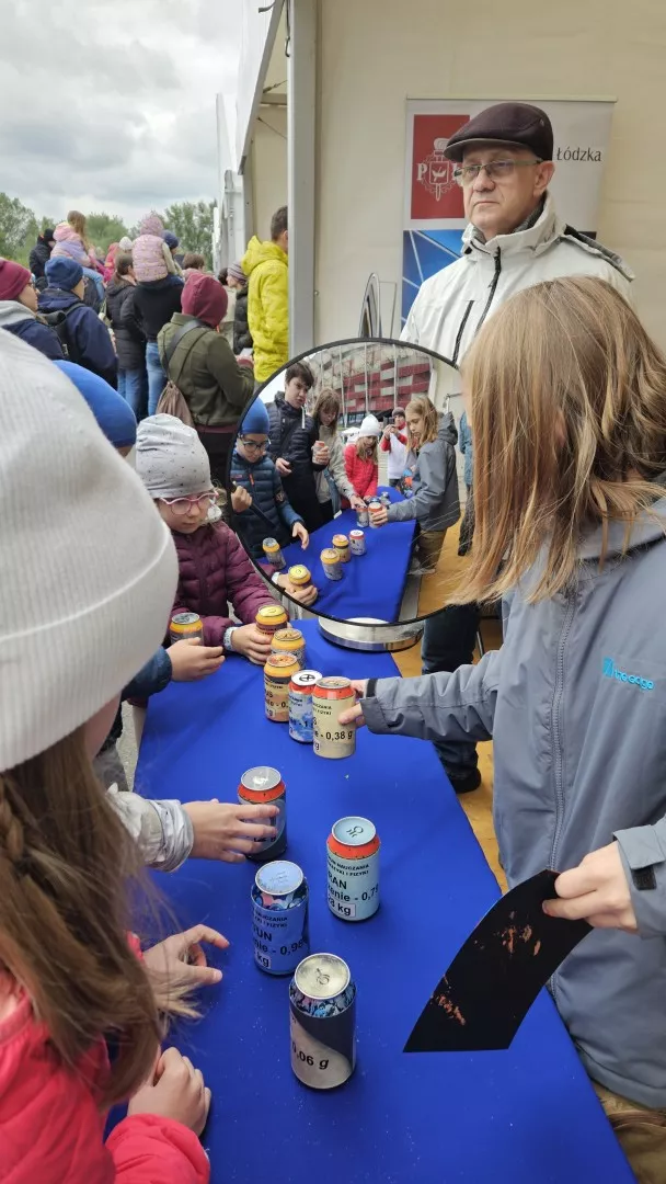 Osoby stojące wokół stołu, na którym stoją różne puszki