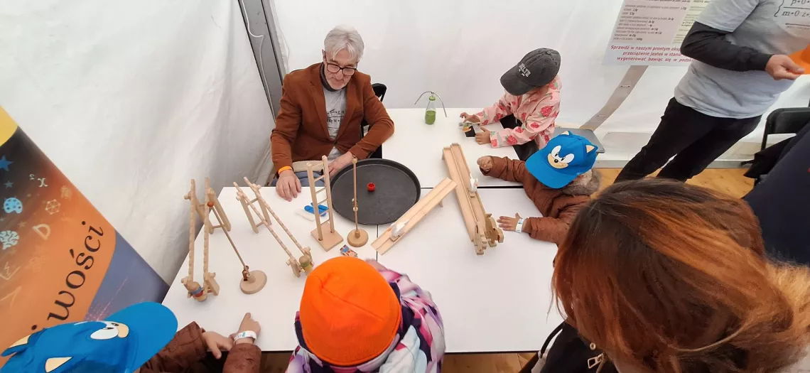 Zabawki drewniane leżą na stole, przy którym siedzą dzieci