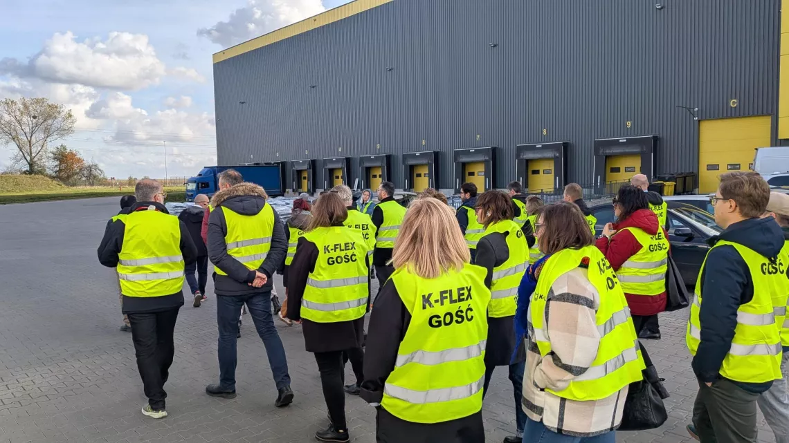 Grupa osób w żółtych kamizelkach zwiedza teren zakładu przemysłowego
