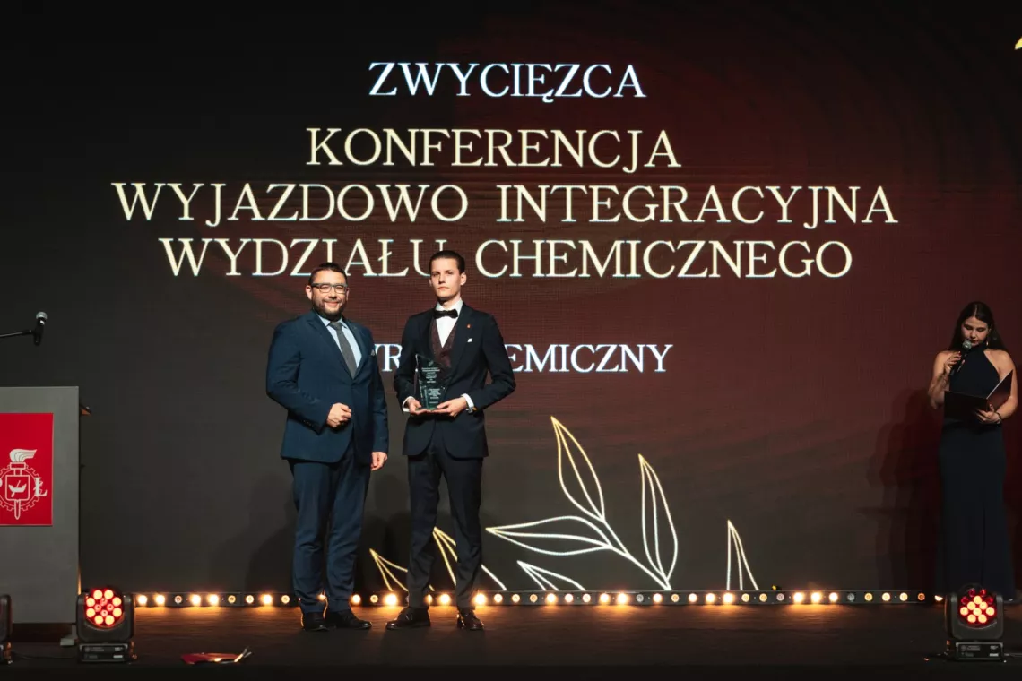 Dwóch mężczyzn, jeden trzyma statuetkę, z tyułu napis Zwycięzca konferencja wyjazdowo integracyjna wydziału chemicznego