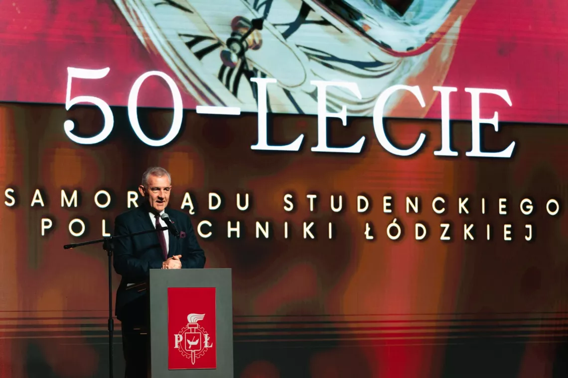 Mężczyzna przy pulpicie przemawiający do mikrofonu, z tyłu napis 50-lecie Samorządu Studenckiego Politechniki Łódzkiej
