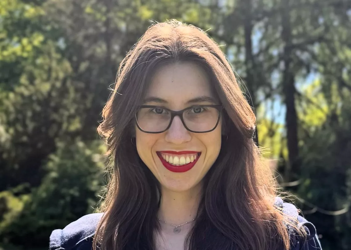 Twarz młodej kobiety z długimi włosami, w okularach. Jest szeroko uśmiechnięta