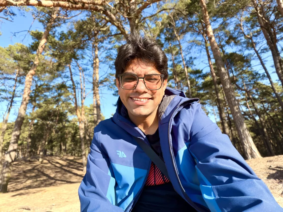 Uśmiechnięty mężczyzna w okularch i sportowej kurtce, w tle zielony las