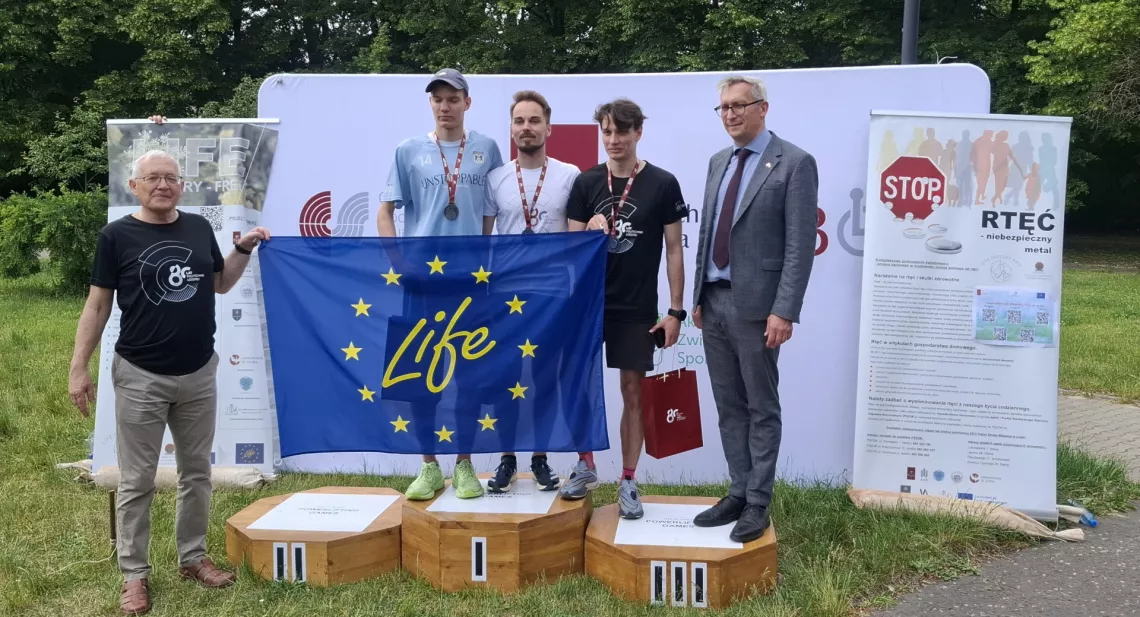 Trzech stoi na podium, trzymając unijna flagę z napisem life, obok mężczyzni, którzy wręczali nagrody