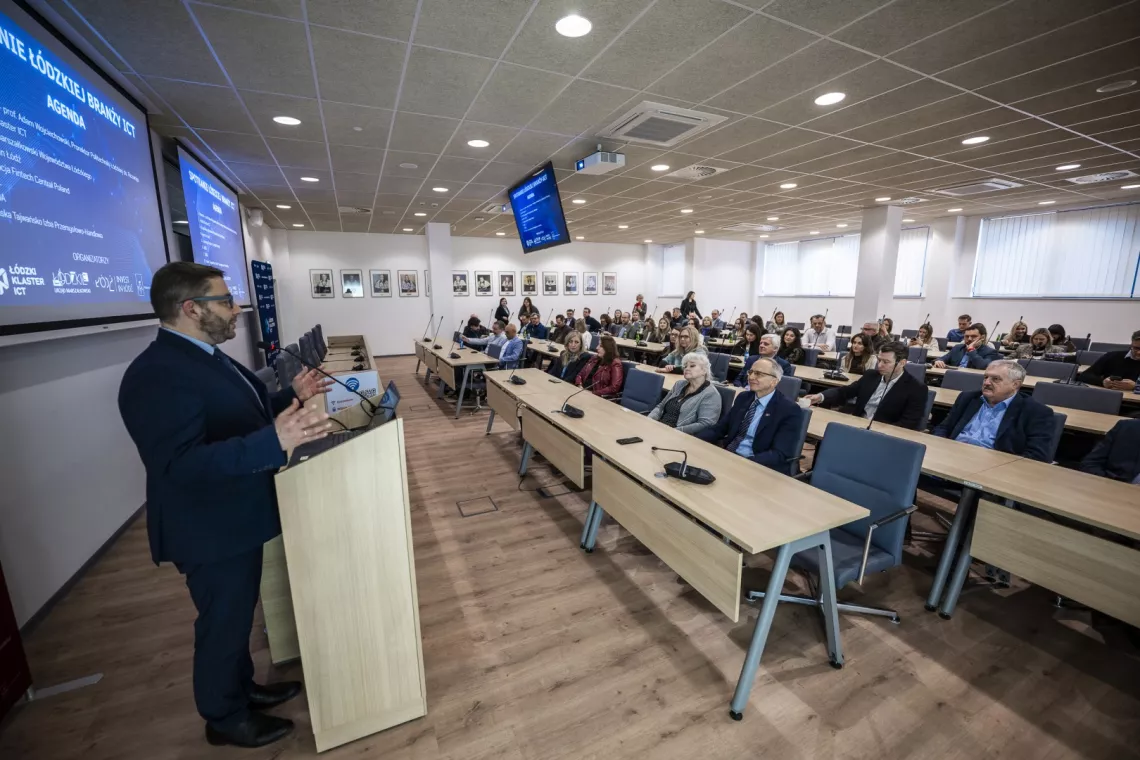 Mężczyzna przemawia przy mównicy do zebranych w sali