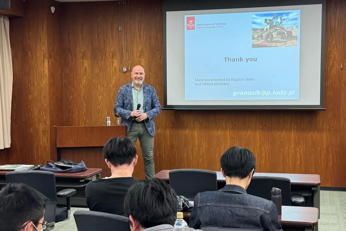 Osoba stojąca przed ekranem prezentacyjnym w sali wykładowej. Na ekranie widnieje slajd z napisem:  "Dziękuję  Materiały dostarczone przez zespół Raptors i firmę Hololot