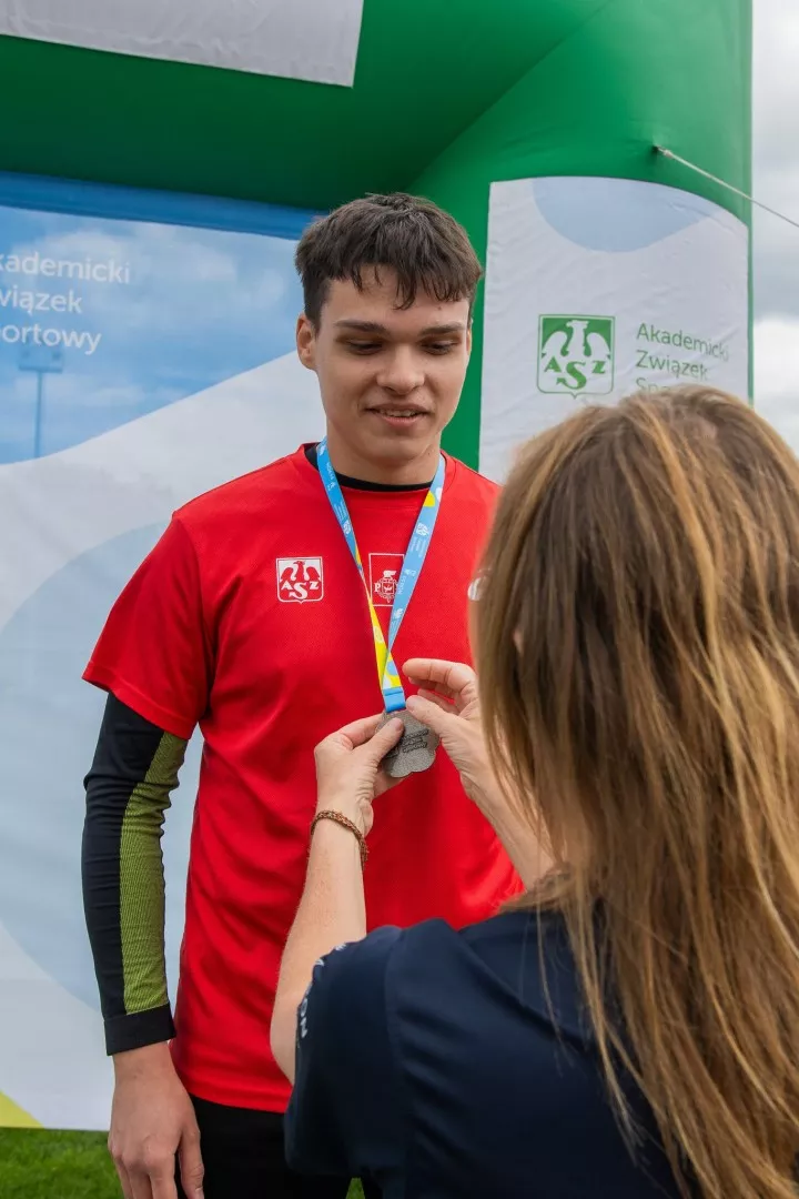 Kobieta zawiesza medal sportowcowi w czerwonej koszulce