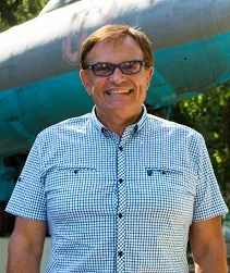 Mężczyzna w koszuli z krótkimi rękawami , w ujęciu do pasa,  z usmiechem na twarzy