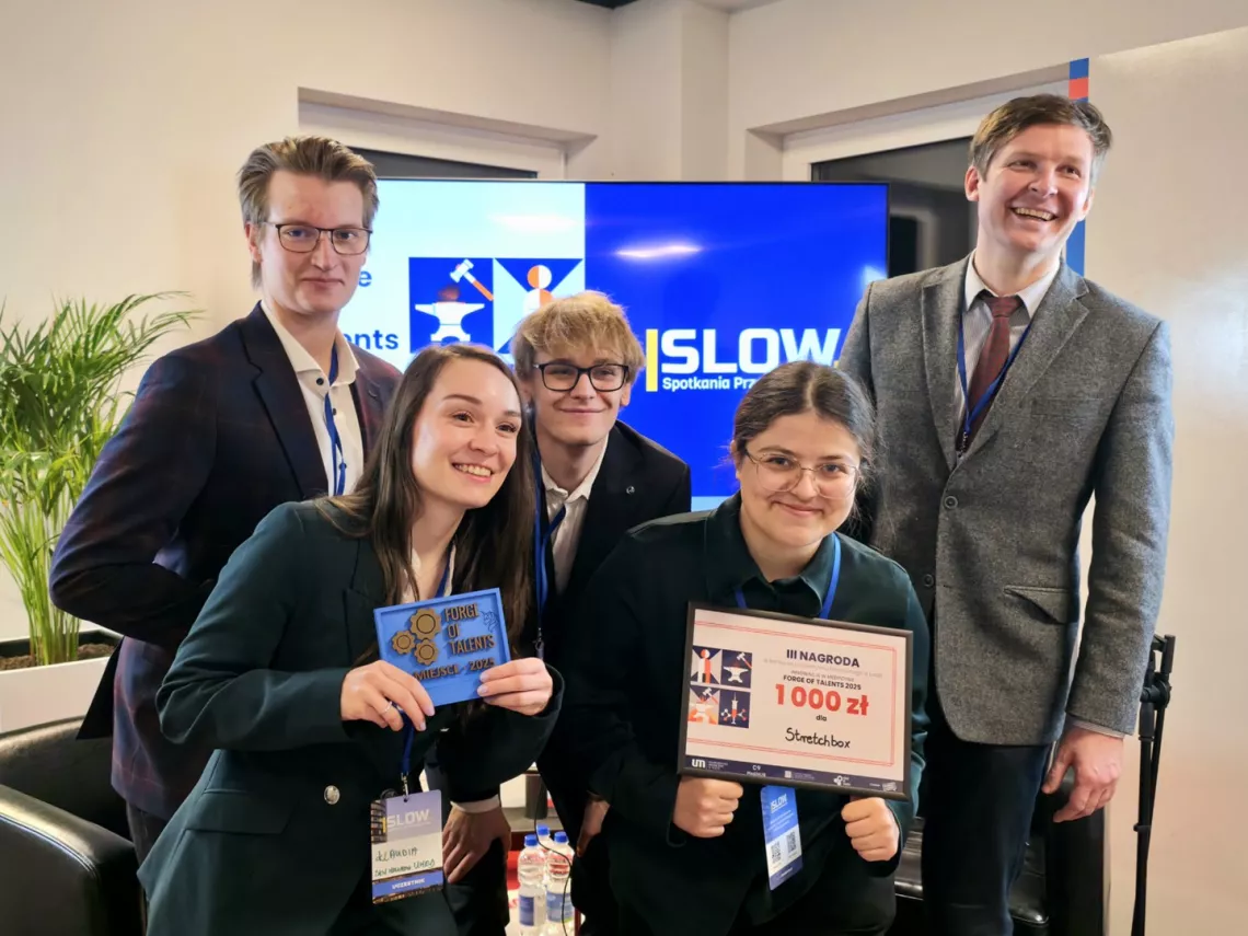 Piecioro młodych osób uśmiechniętych i radosnych z powodu ptrzymania nagrody, którą jedna z nich trzyma w ręku