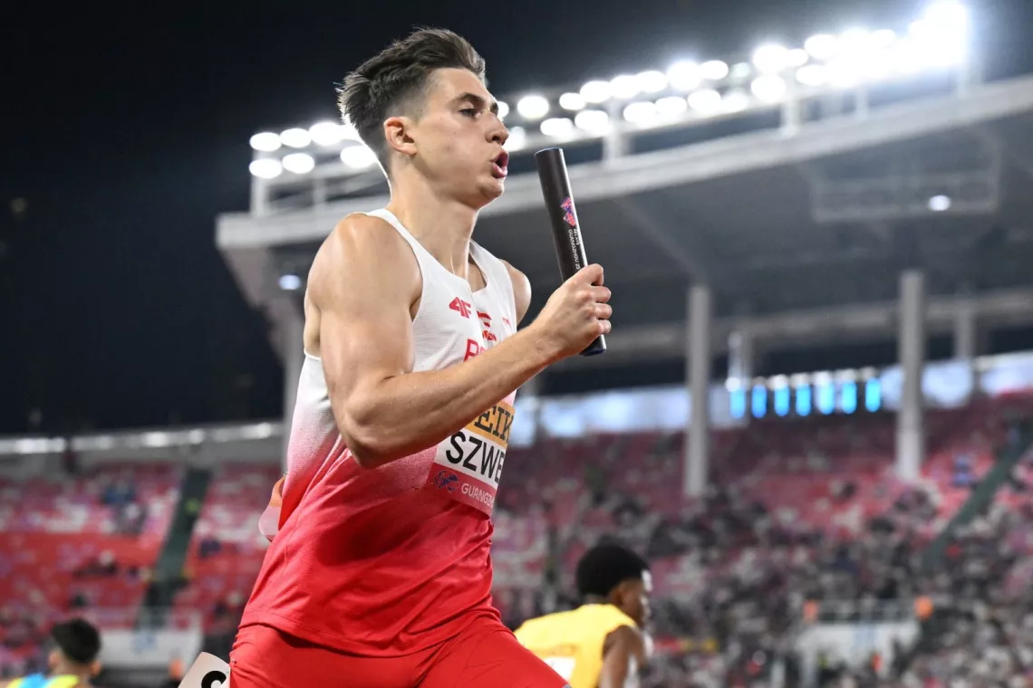 Sportowiec w biało-czerwonym stroju z pałeczką w ręku w czasie biegu sztafetowego