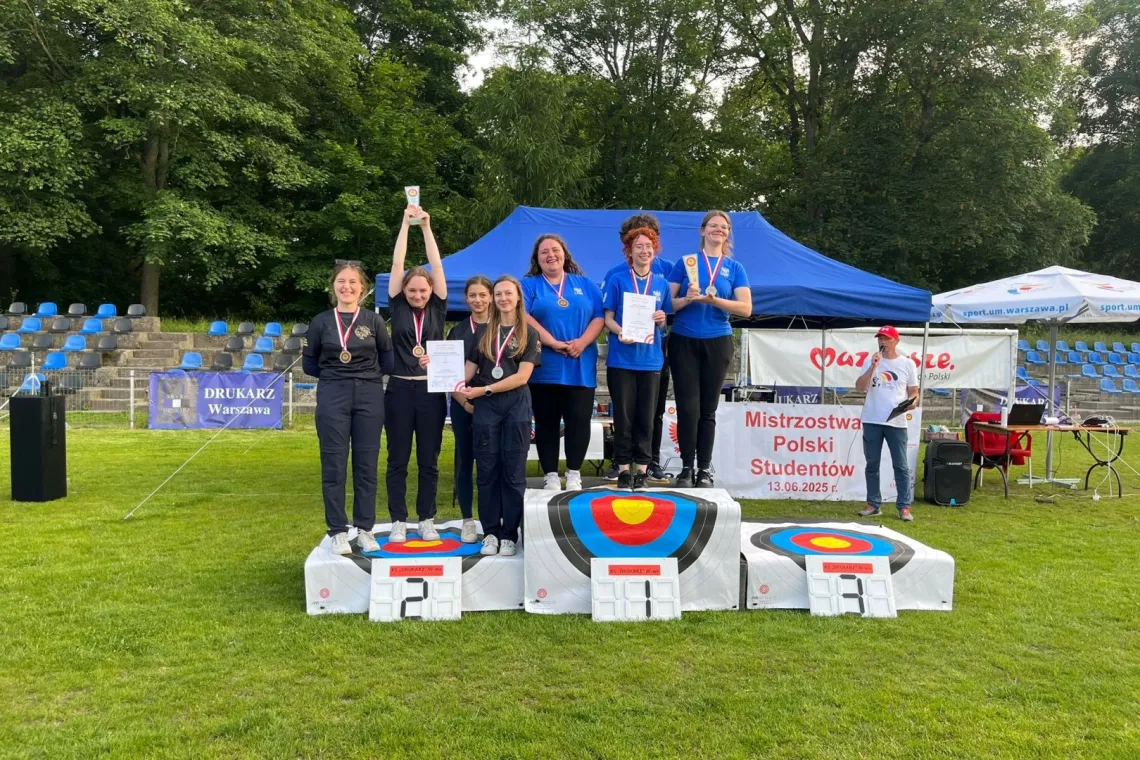 Zawodniczki stoją na podium, w tle namiot, trybuny oraz drzewa