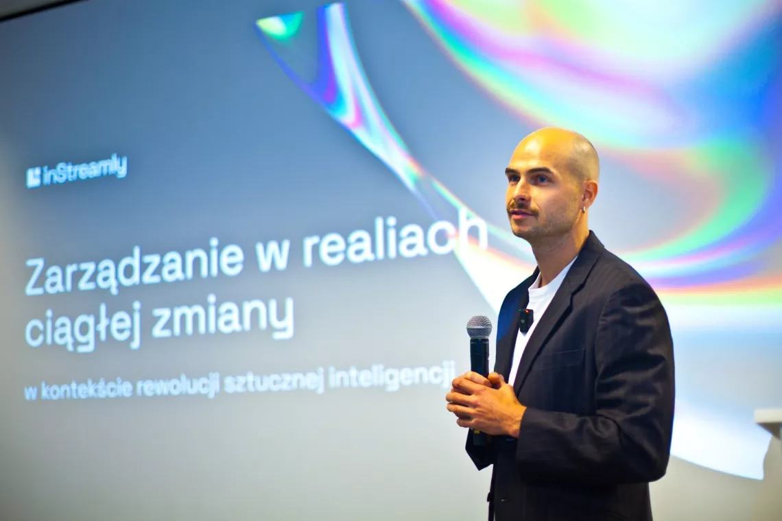 Mężczyzna z mikrofonem soi na tle dużego ekranu, na którym widać tytuł wykładu