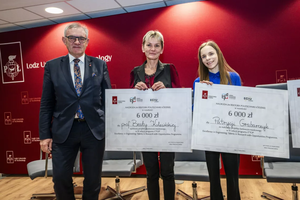 Męzczyzna w garnituzre stoi obok dwóch kobiet trzymających w ręach czeki