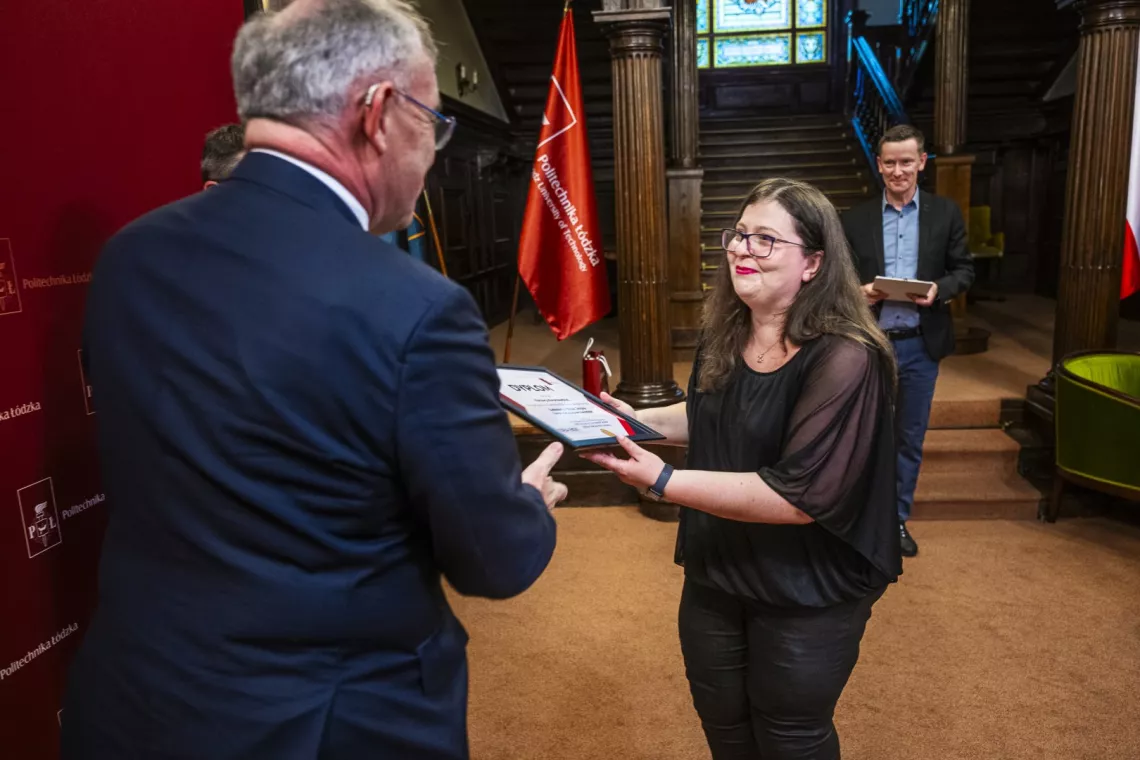 Kobieta odbiera dyplom z rąk mężczyzny stojącego tyłem do obiektywu
