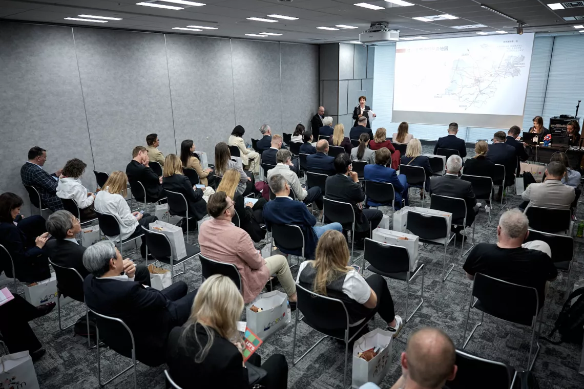 Grupa osób siedzi w sali seminaryjnej, patrząc na przemawiającego i umieszczony za nim ekran