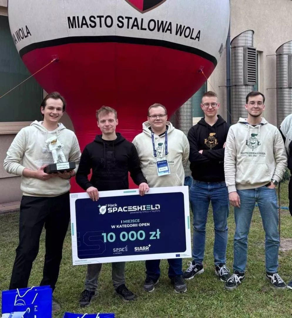 Pięciu młodych mężczyzn stoi przed balonem z napisem Miasto Stalowa Wola. Jeden z nich trzyma duży czek na 10000 zł, a kolejny statuetkę z postacia kosmonauty