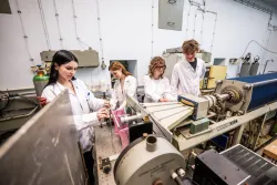 Młode osoby w białych fartuchach pracują przy urządzeniu znajdującym się w laboratorium.