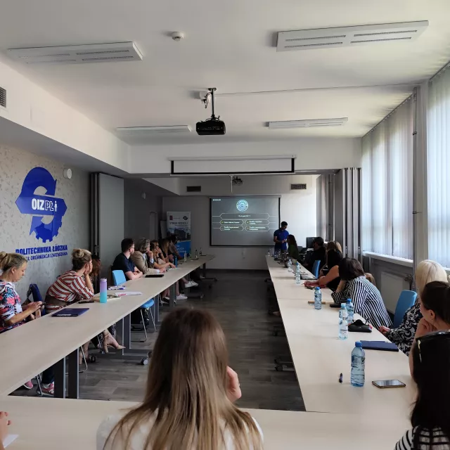 Uczestnicy spotkania siedzą pzry stole w kształcie litery U