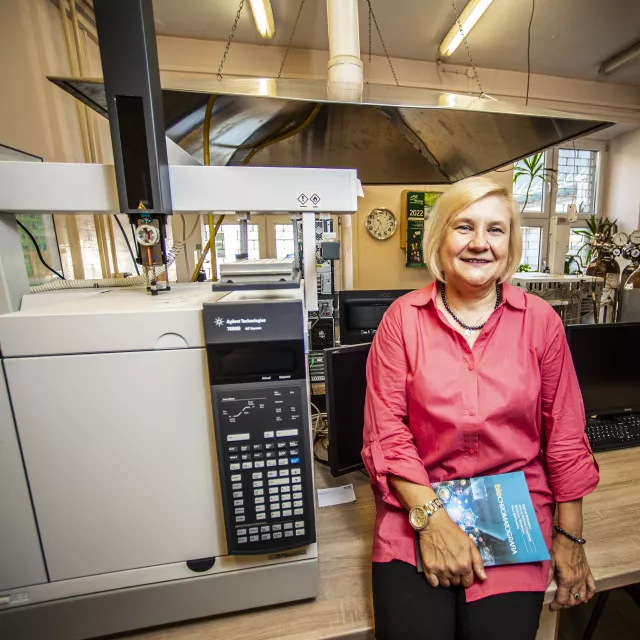 Uśmiechnięta kobieta z książką w ręku stoi pzry sprzęcie w laboratorium