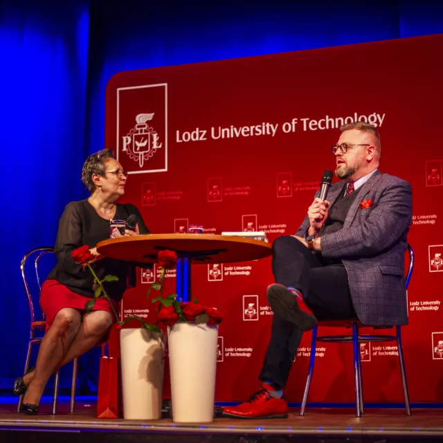 Wywiad prowadzony przy stoliku na tle ścianki z napisem  Politechnika Łódzka