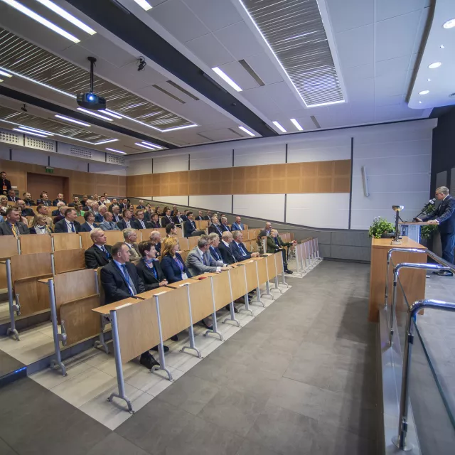 Oosba pzremawiająca z mównicy do licznego grona siedzącego w audytorium