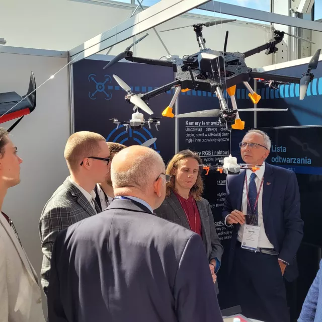 Kilka osób stoi na stoisku Centrum Badawczego Obronności i Bezpieczeństwa PŁ