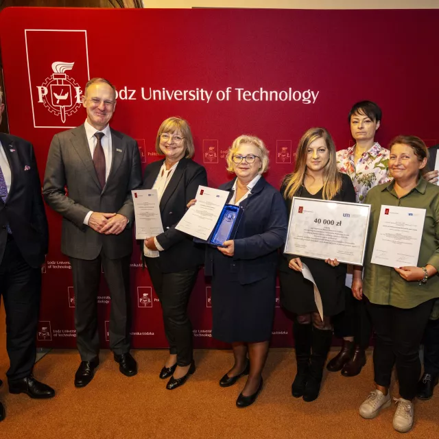 Osiem osób stoi na tle ścianki z napisem Lodz University of Technology, sześć z nich trzyma dyplomy, a także symboliczny czek i statuetki