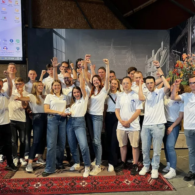 liczna grupa młodych ludzi stoi z rękoma uniesionymi do góry w geście zwycięstwa